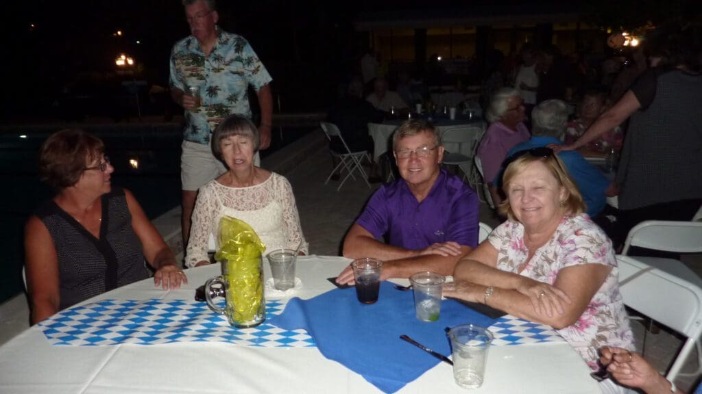 A group of elderly friends sitting around a table at an evening event.