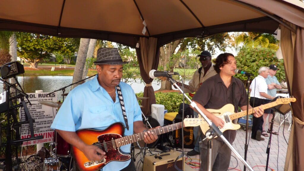 Two musicians playing electric guitars outdoors under a canopy.