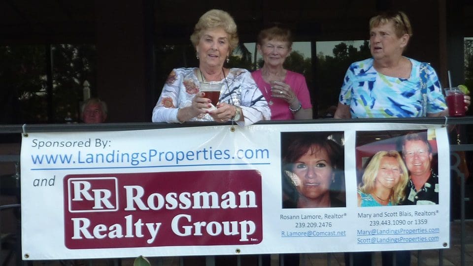 Two women holding a realty group banner at an outdoor event.