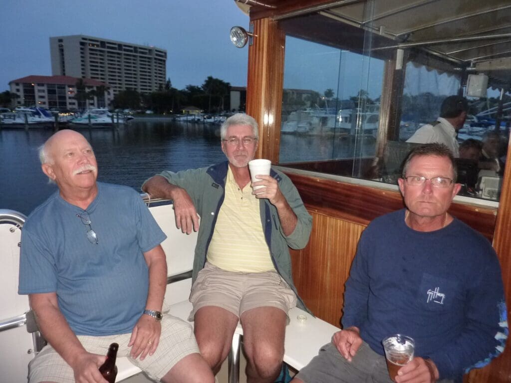 Three men relaxing on a boat in casual clothes with a waterfront view.