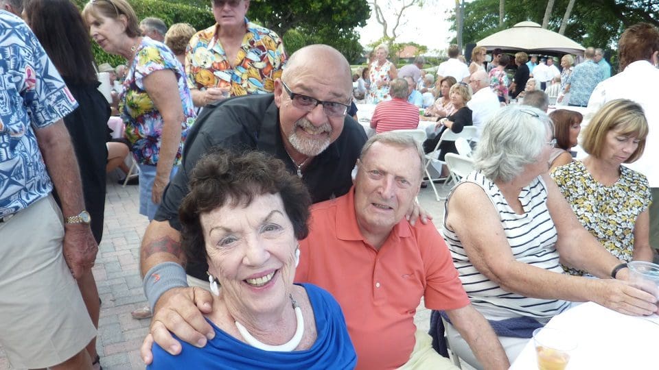 Three smiling adults enjoying an outdoor gathering.