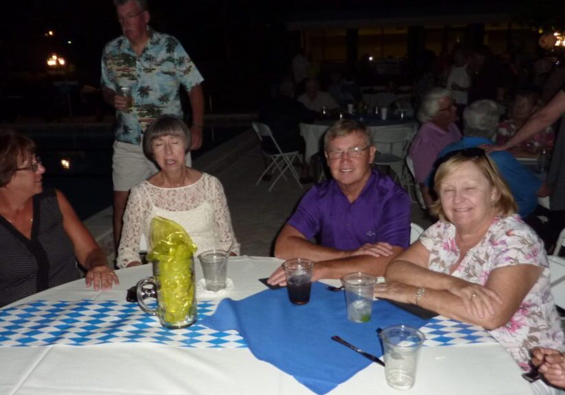 A group of elderly friends sitting around a table at an evening event.