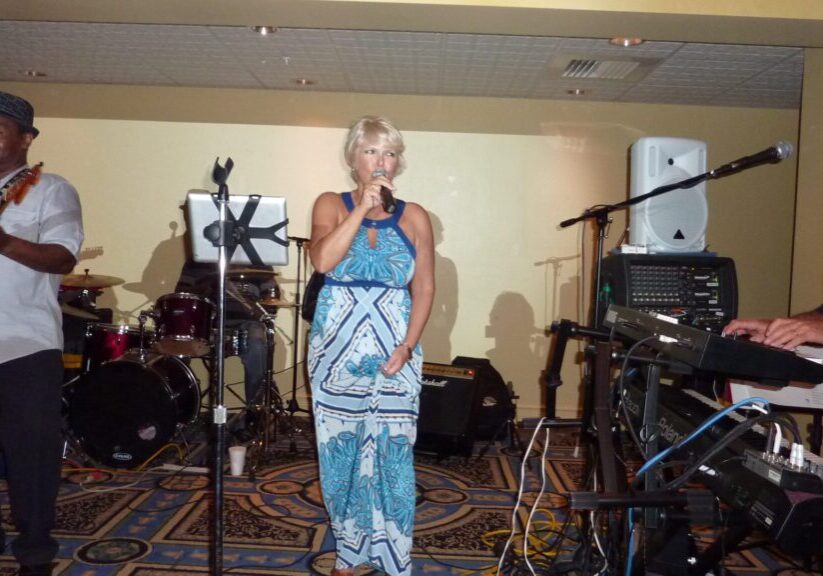 Woman singing on stage with microphone and musical instruments in background.