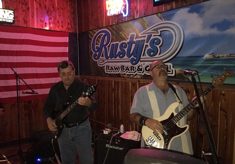 Two musicians play guitars on a dimly lit stage at Rusty's Bar and Grill.
