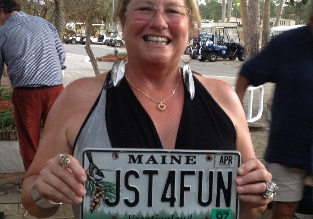 Woman proudly holds a Maine license plate with the message 'JST4FUN'.