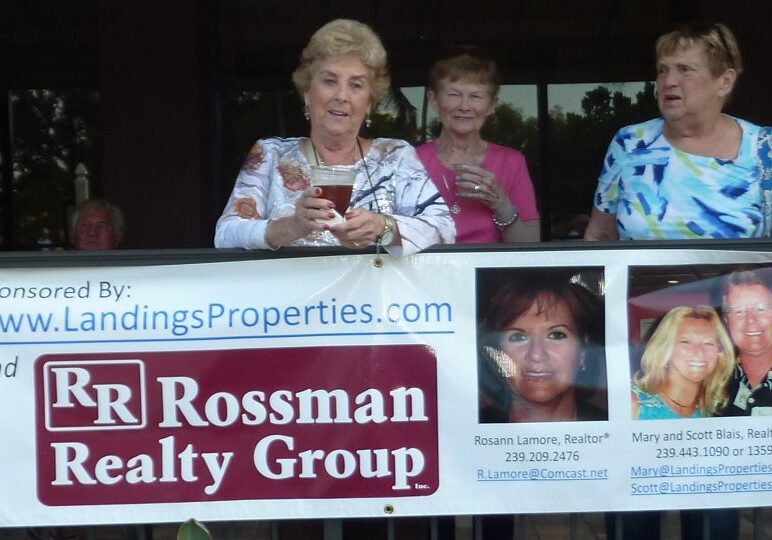 Two women holding a realty group banner at an outdoor event.