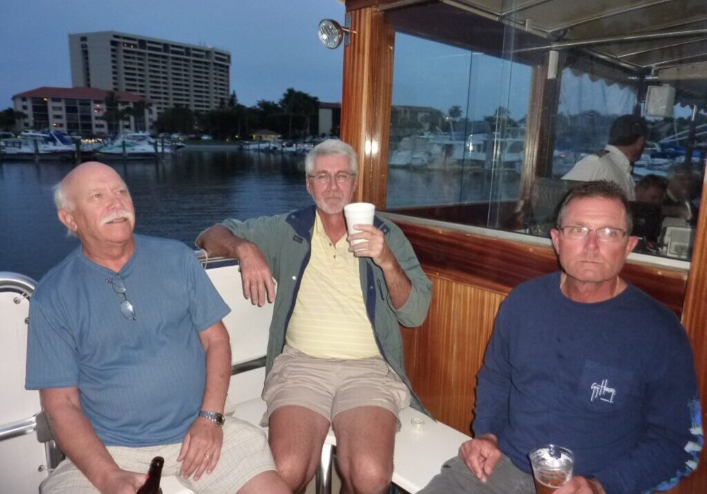 Three men relaxing on a boat in casual clothes with a waterfront view.