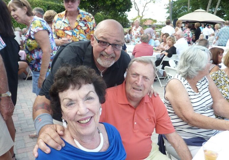 Three smiling adults enjoying an outdoor gathering.